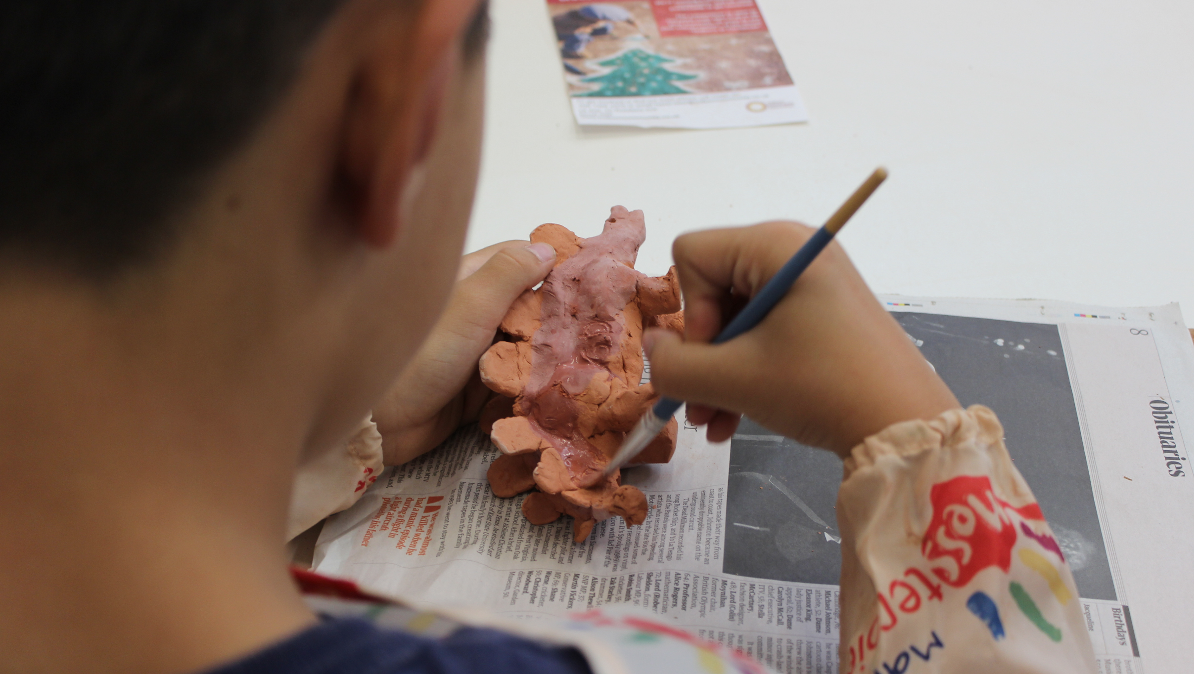  close up of a boy painting a brown ceramic dinosaur