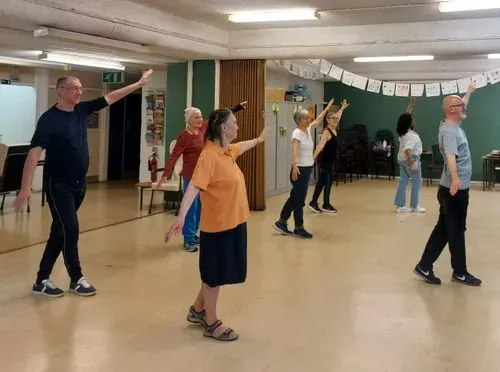 Six older adults and an instructor are dnacing with their arms held in a diagonal position.