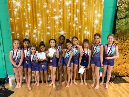 A group of gymnasts showcasing their medals and certificates obtained at a squad competition