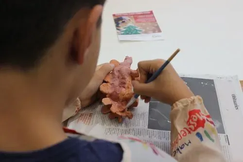 Image of a boy painting a ceramic dinosaur with a paintbrush