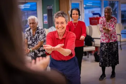 A diverse group of four, smiling adults aged 55 and over perform a South Asian dance hand gesture.