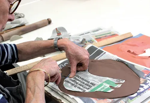 Image of someone drawing round a newspaper template on a piece of clay