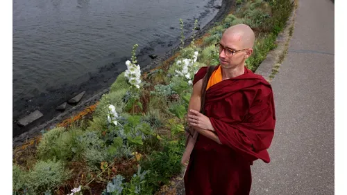 The facilitator, a Buddhist monk, standing by the river bank in a contemplative pose