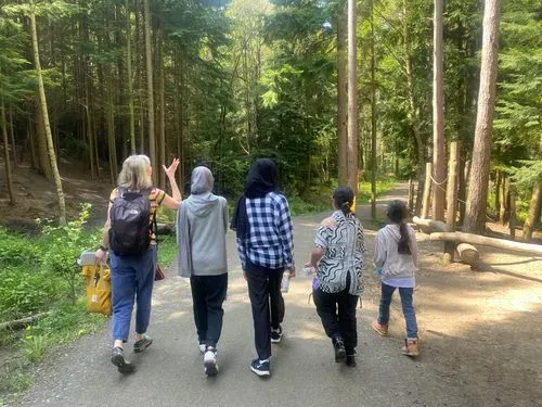 An adult walking in the forest with 4 children all seen from behind. 