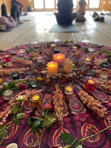 a mandala containing candles and flowers laid out on a floor in a yoga studio with people sitting on mats in the distance. 