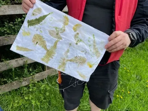 hands holding up a piece of material with leaf prints on from doing hapa-zome. 