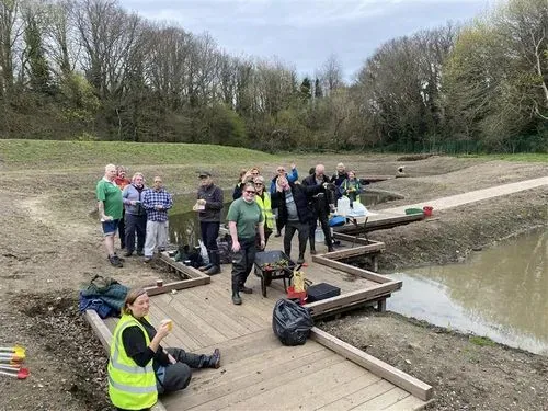 Volunteers smile and wave standing on a boardwalk by the ponds