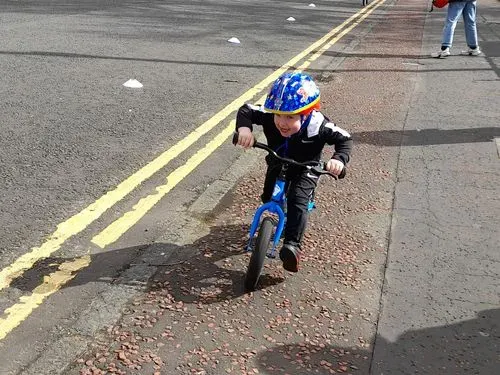 A young boy learning to ride a bike. He is smiling. An adult is helping him