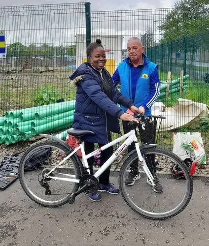 A woman and a man standing with a bike. The woman has just learned to ride the bike.