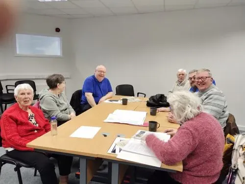 Group members are sat round a table smiling while looking at old maps of South Shields.