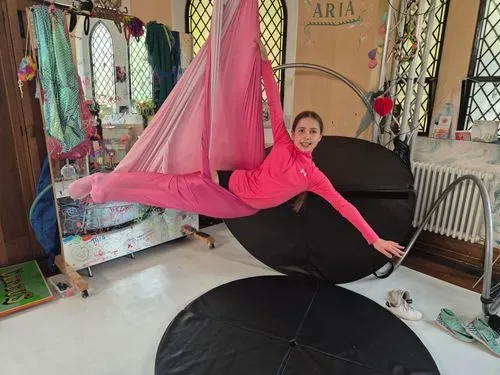 A young girl in a pink aerial hammock in mermaid pose