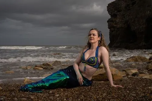 A woman on the beach in a green mermaid tail. Try on our mermaid tails!