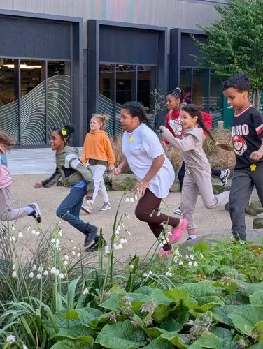 Children excitedly running in between flower beds and a grey building.