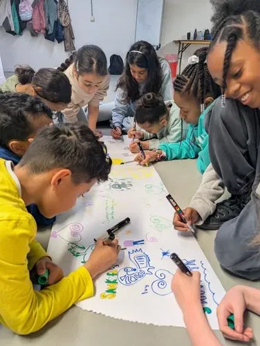 Children in brightly coloured clothes, gathered around a long sheet of paper writing ideas and images.