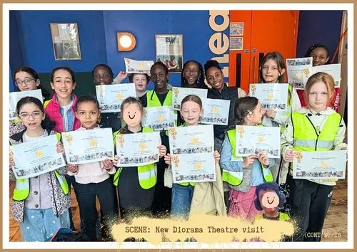 Two lines of children holding white certificates within a red and blue room. A pink bubble describes the picture.