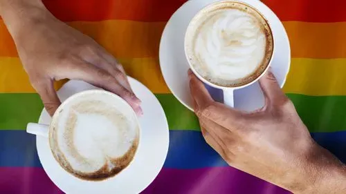 Two cups of coffee being held over a rainbow flag