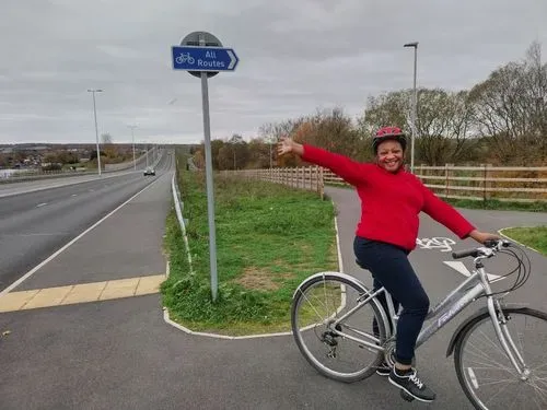 A beautiful woman of African Heritage in a red top and dark bottoms smiling while stationery with a bicycle