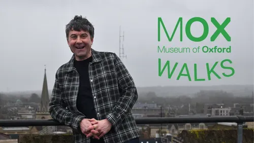 A photo of tour guide Maurice East with the Oxford skyline in the background. He is wearing a grey checkered shirt and smiling.