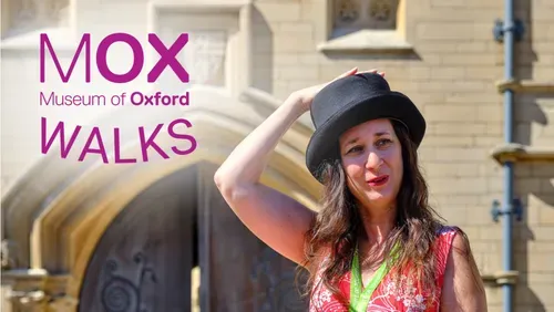 A photo of tour guide Jess Worth against a limestone Oxford building and wooden door. She is wearing a pink dress and a black top hat.