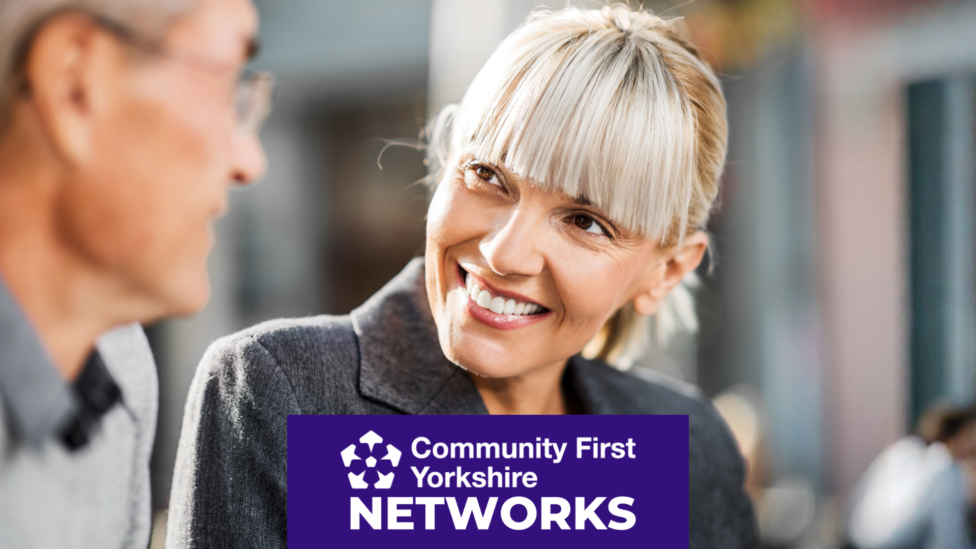 Person wearing a grey jacket in an indoor setting with blurred people in the background. Purple banner reads “Community First Yorkshire NETWORKS.”