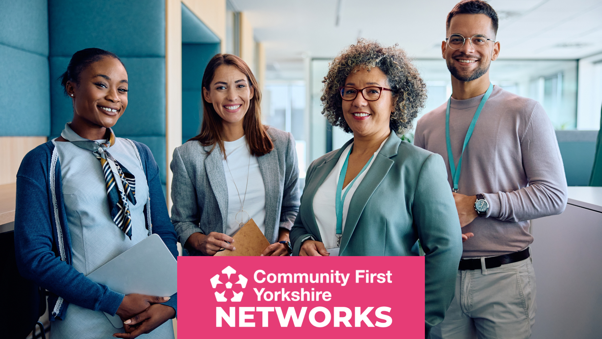 Four people standing in an office setting, wearing business attire and lanyards, holding folders and notebooks. Pink banner reads “Community First Yorkshire Networks.”