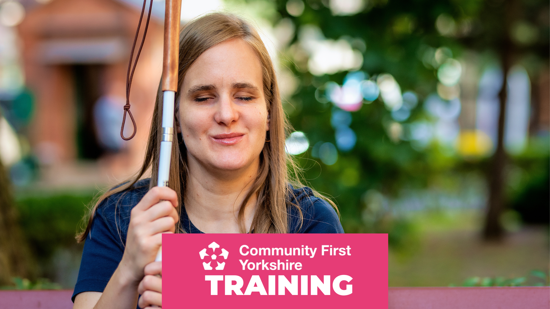 Blind person sitting outdoors holding a white cane with a looped strap. Pink banner reads “Community First Yorkshire TRAINING.”