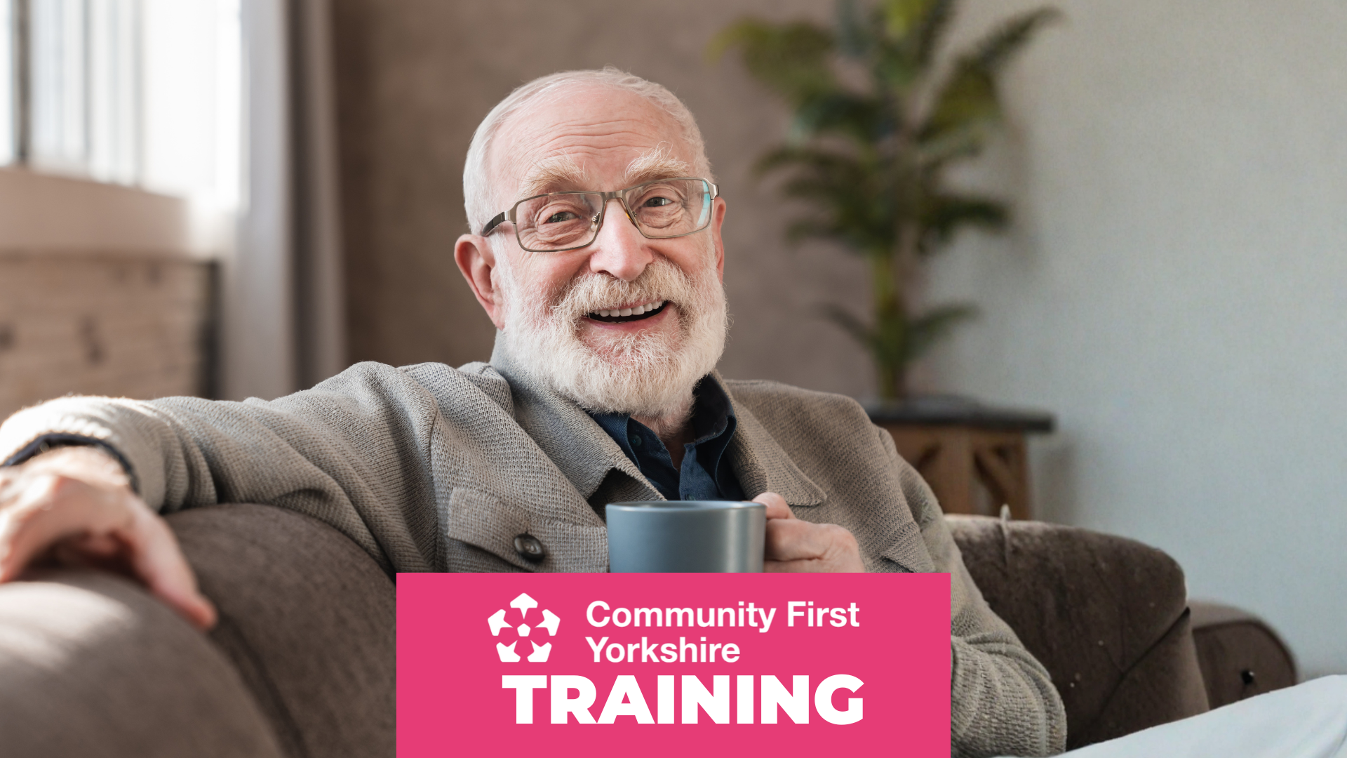 Person sitting on a sofa holding a grey mug, wearing a buttoned cardigan. Background shows a plant and soft natural light. Pink banner reads “Community First Yorkshire TRAINING.”