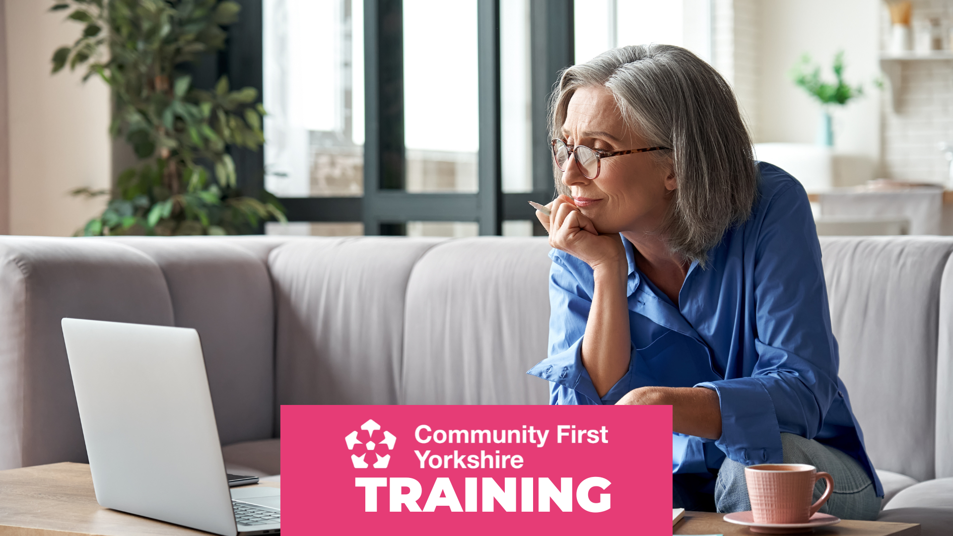 Person sitting on a sofa with a laptop on a coffee table, holding a pen and a cup nearby. Pink banner reads “Community First Yorkshire TRAINING.”