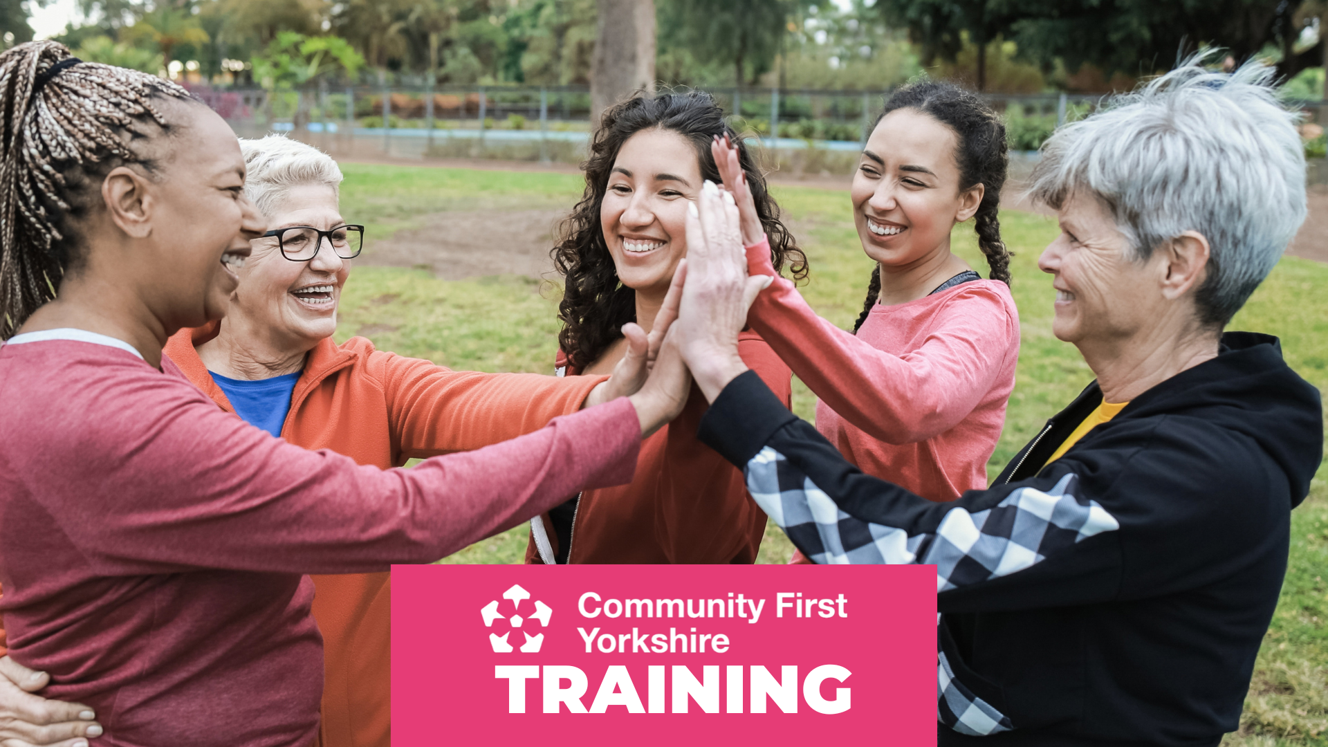 Group of people standing outdoors in a park, forming a circle and touching hands together in the center. Pink banner reads “Community First Yorkshire TRAINING.”