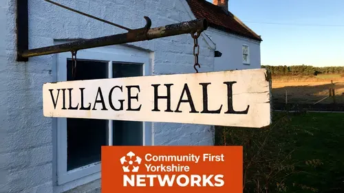 Sign reading ‘Village Hall’ hanging outside a white building with Community First Yorkshire Networks logo.