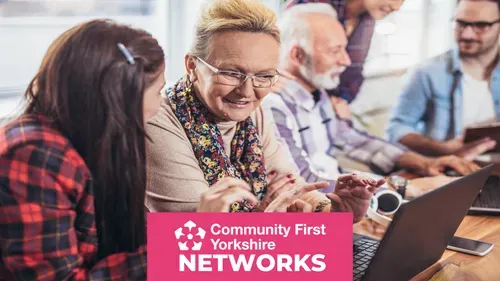Group of people sitting around a table with laptops and notebooks, engaged in discussion. Pink banner reads “Community First Yorkshire NETWORKS.”