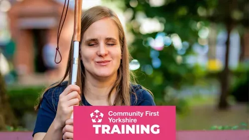 Blind person sitting outdoors holding a white cane with a looped strap. Pink banner reads “Community First Yorkshire TRAINING.”