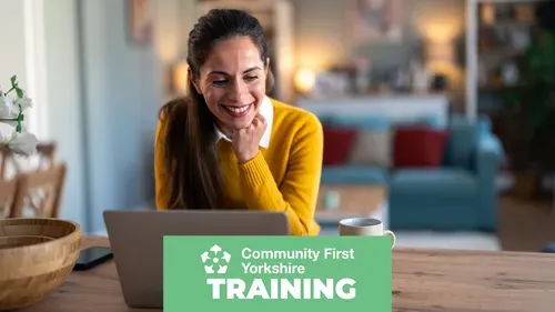 Person sitting at a wooden table using a laptop, with a mug nearby. Background shows a living room with a sofa and cushions. Green banner reads “Community First Yorkshire TRAINING.”