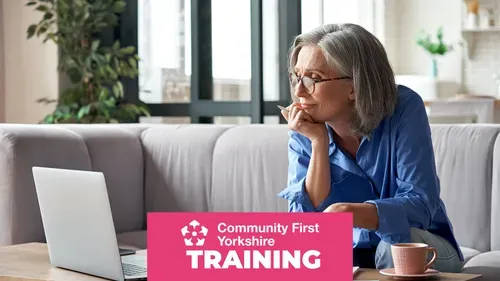 Person sitting on a sofa with a laptop on a coffee table, holding a pen and a cup nearby. Pink banner reads “Community First Yorkshire TRAINING.”