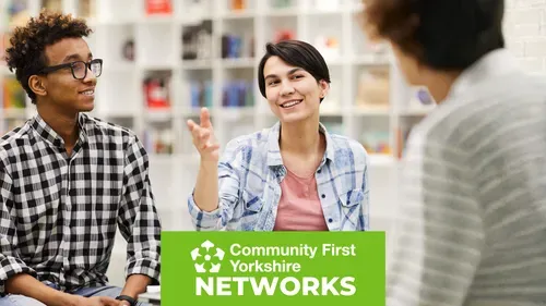 Three people sitting and talking in a bright indoor space with shelves of books in the background. One person is gesturing with a raised hand. Green banner reads “Community First Yorkshire Networks.”