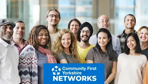 Group portrait of several people standing together indoors, with a Community First Yorkshire Networks logo displayed in the foreground.