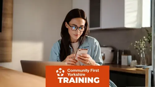 Person wearing glasses using a smartphone while sitting at a table with a laptop in a home setting. Community First Yorkshire Training branding is displayed across the bottom of the image.