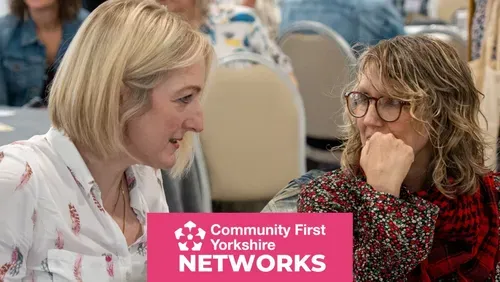 Two people are seated and talking at a community networking event, with a "Community First Yorkshire Networks" banner displayed in the foreground.