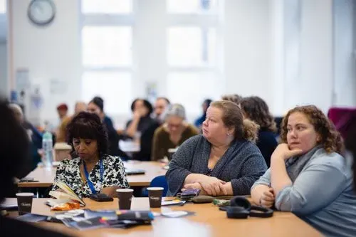 In this image there are three women, one looking down, one looking to the side and one looking straight ahead with one arm up to her face