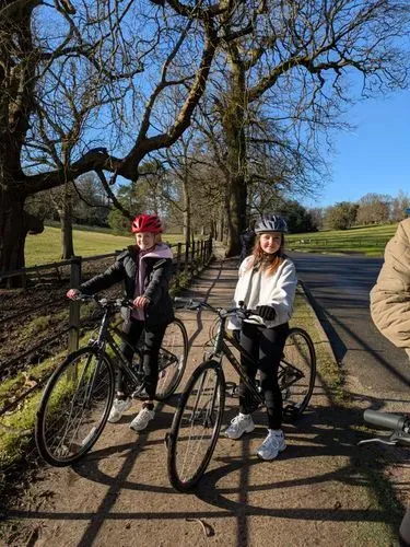 Two teenage girls on bikes with trees and blue sky behind them
