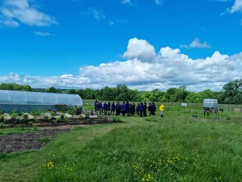 A group of students on the GROW Farm on a sunny day, stood next to a polytunnel.