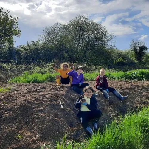 Four young people sat on the Grow farm's compost heap smiling and waving.