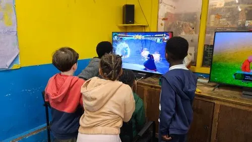 four children gather round a large tv screen watching friends play a computer game