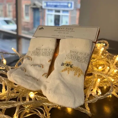 Inside of a shop, there is shelve unit full of potential presents. There is a decorative plan on top anda label reading GIFT SWAP