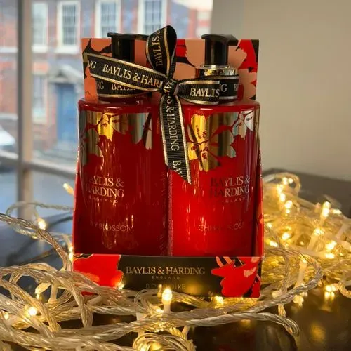 Inside of a shop, there is shelve unit full of potential presents. There is a decorative plan on top anda label reading GIFT SWAP