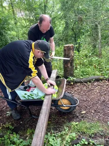 Two green gym volunteers working as a team to measure and cut a plank of wood to refurbish some steps on one of our woodland paths.