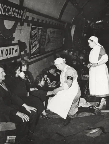 A historic black-and-white photograph showing St John Ambulance volunteers providing first aid to civilians sheltering at Piccadilly Underground station during the Second World War.