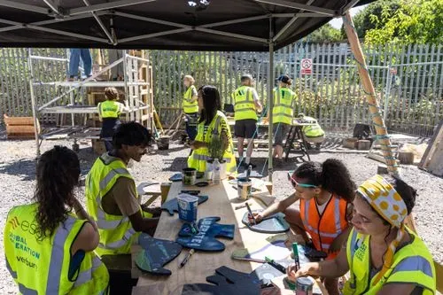 People sat at a table in the sunshine painting signs for our hoarding