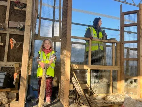 A child in high visibility vest on a cob wall